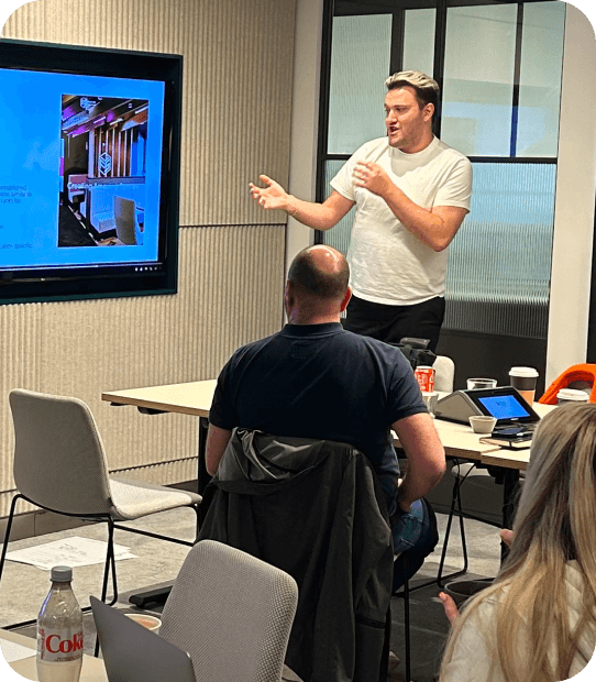 man stood up in a room talking at a screen