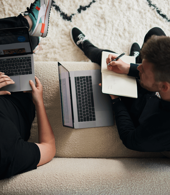 two men sat on a sofa both with laptops